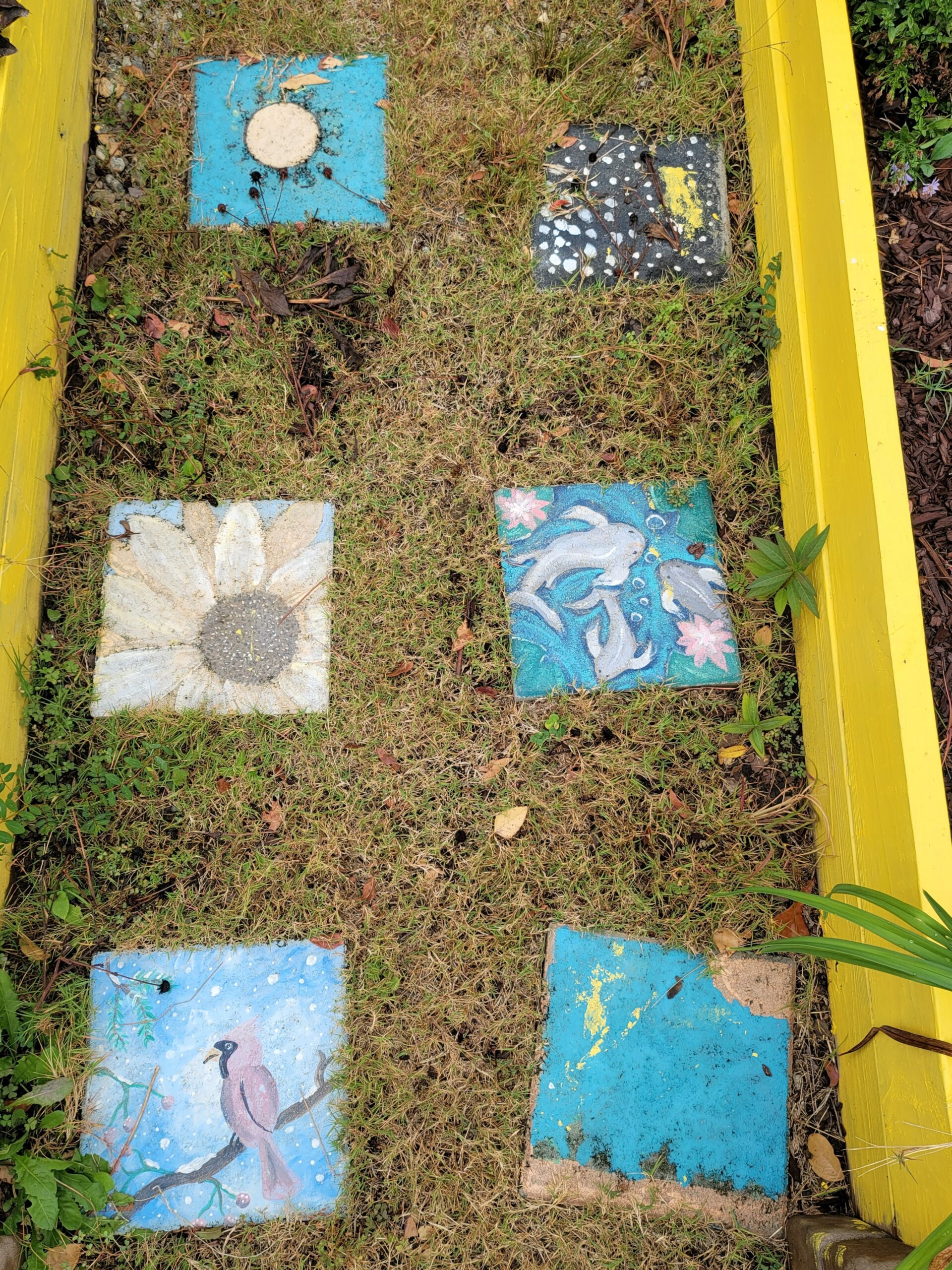 Overhead shot of six painted stepping stones, set in grass.