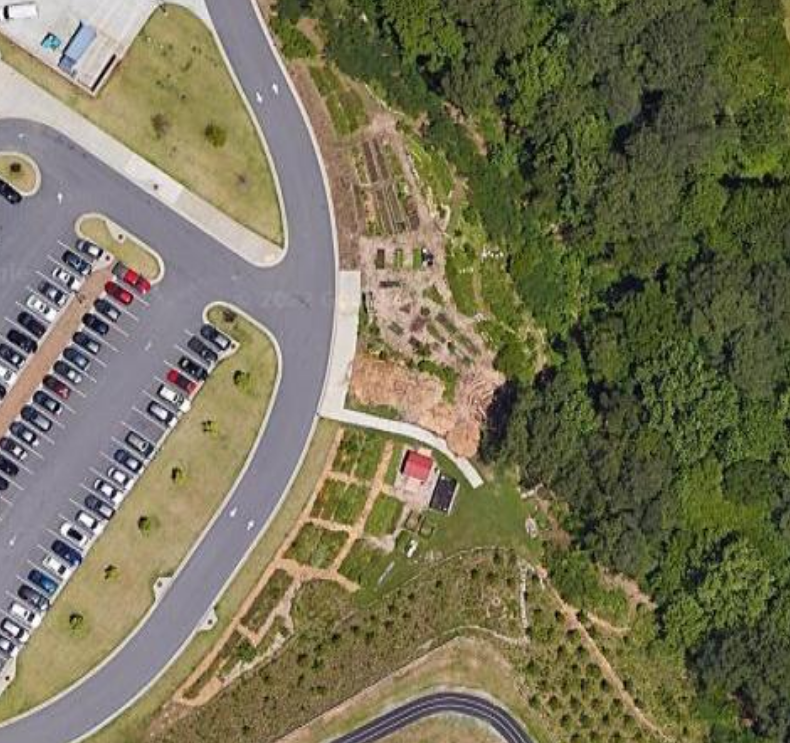 Satellite view of a parking lot with a crescent-shaped landscaped border, with a green forest beyond.