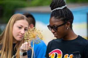 Two students look closely at a pretty, firework-like allium flower.