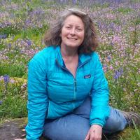A woman in teal sits in front of a meadow of purple and white flowers,