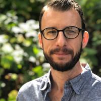 Photo of a person in dark glasses and beard and a blue shirt.