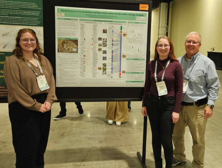 Three people stand smiling next to a large poster indoors.