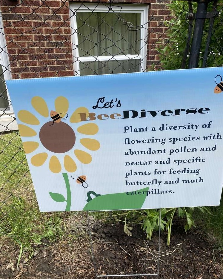 A yard sign with an illustration of a been and flower with black text.
