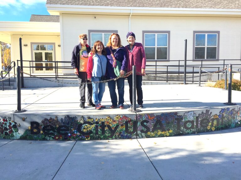 Four people stand above a glass mural reading Bee City USA Talent.