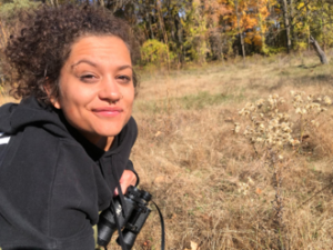 A smiling person holding binoculars in a golden field.