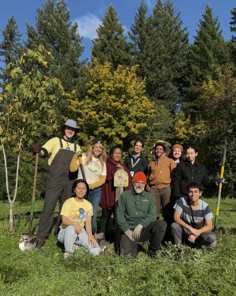A group of ten people stand and kneel outdoors in work clothes.