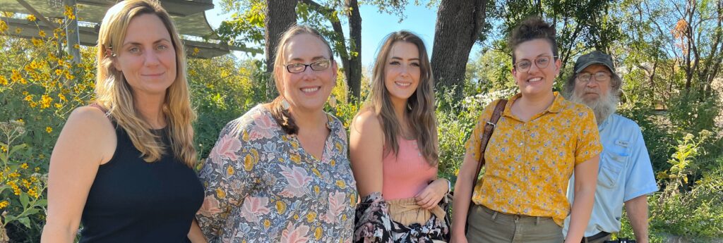 Five people smile in front of yellow flowers.
