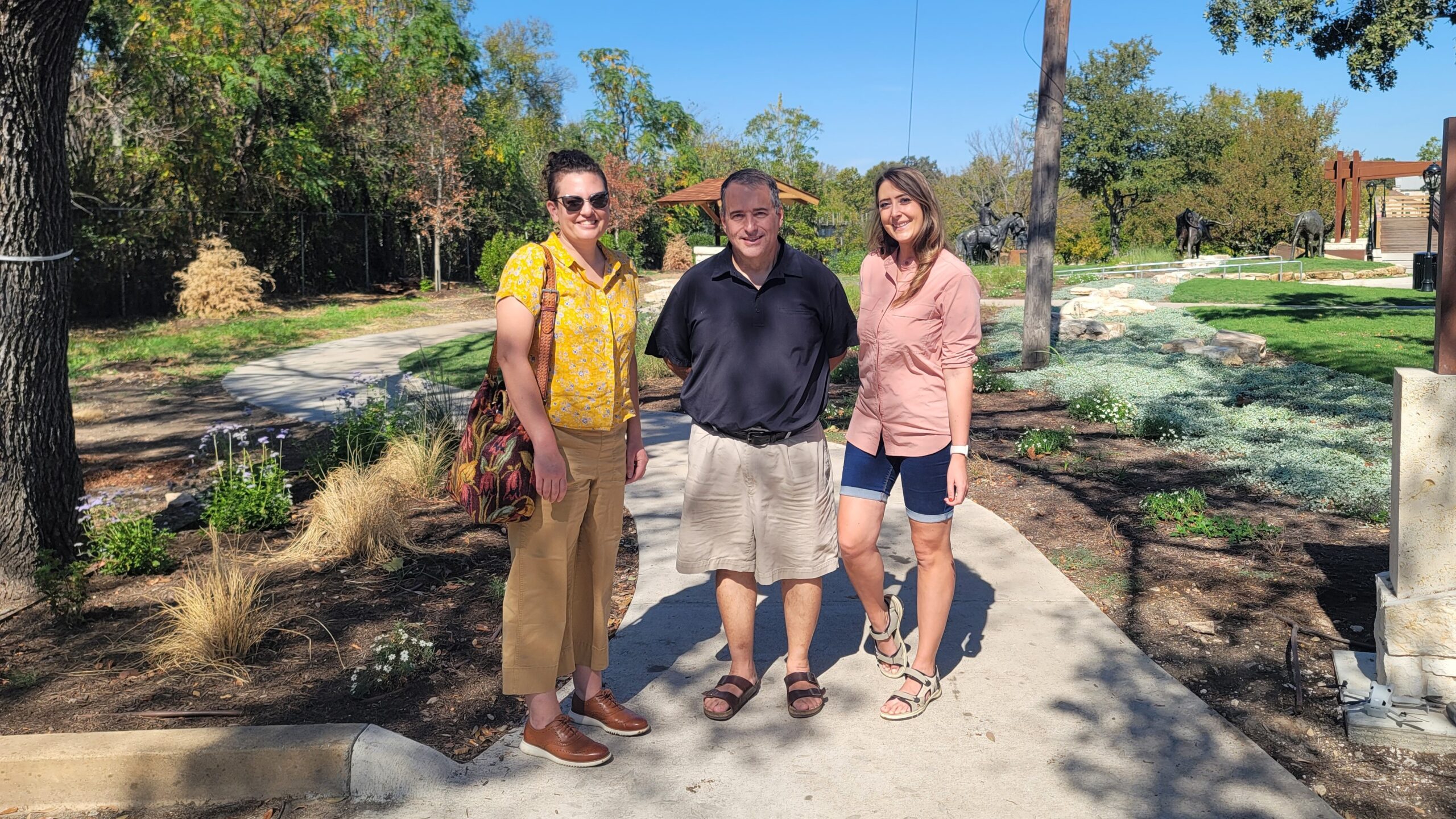Three people stand smiling in a path path with short green plants in the background.