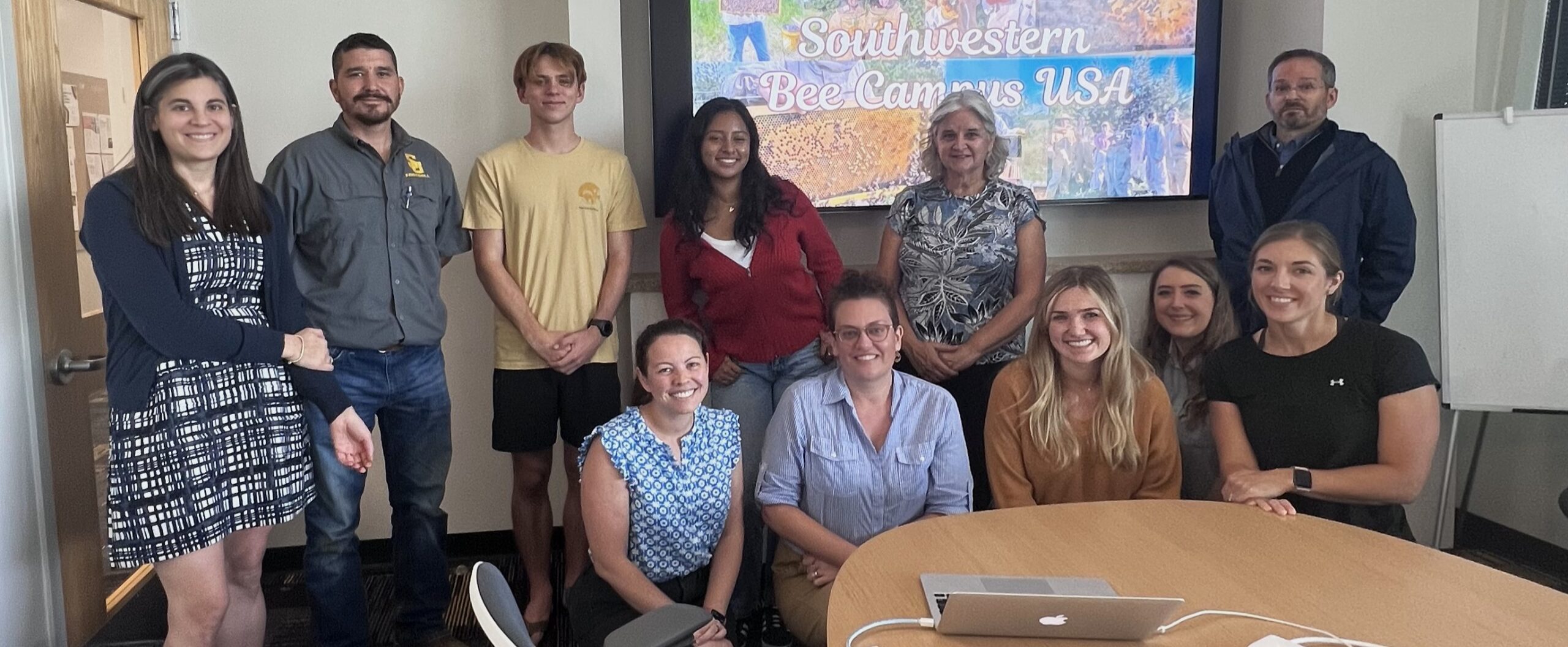 11 people pose smiling in front of a presentation screen.