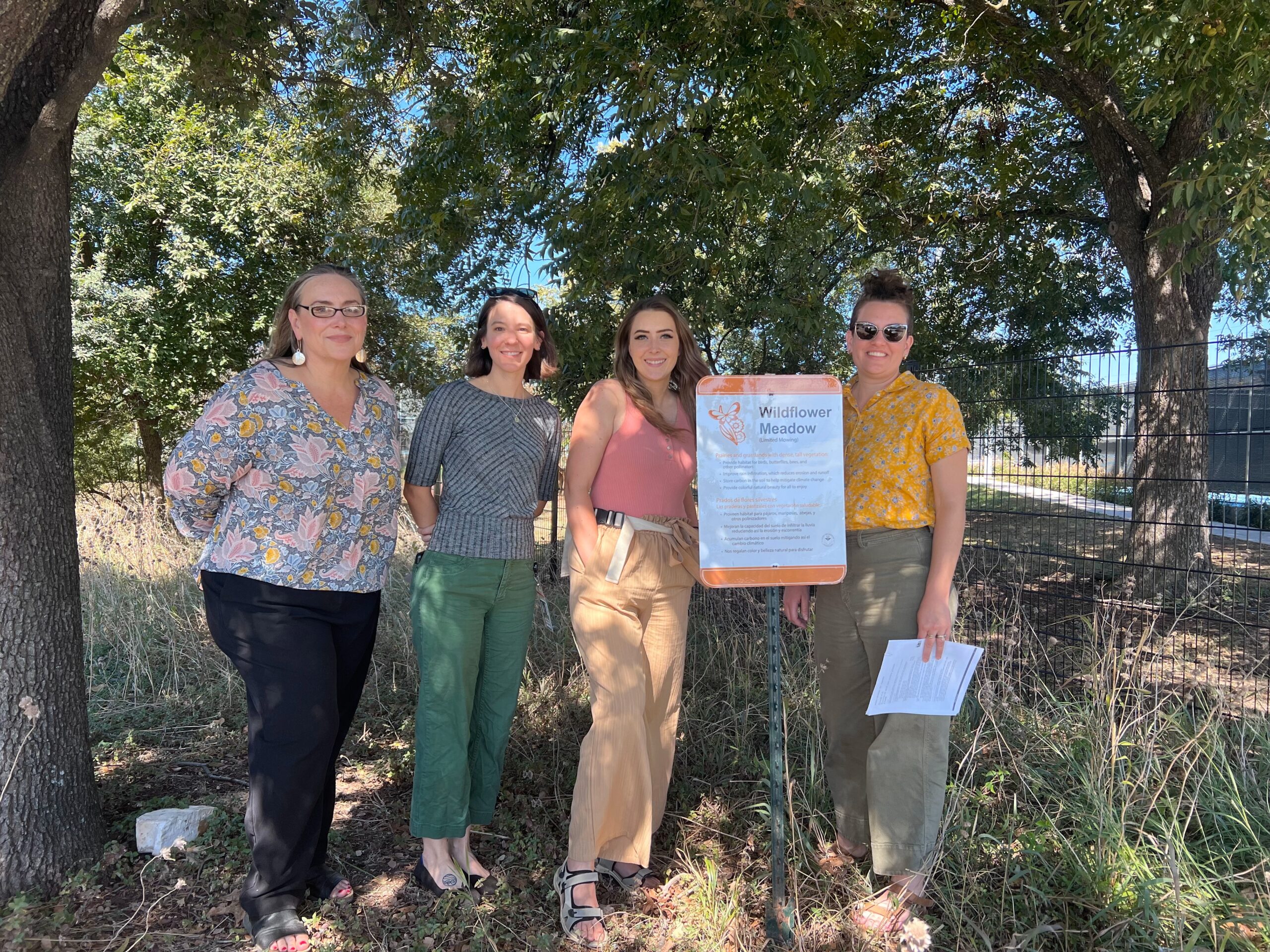 Four people pose next to a sign outside.
