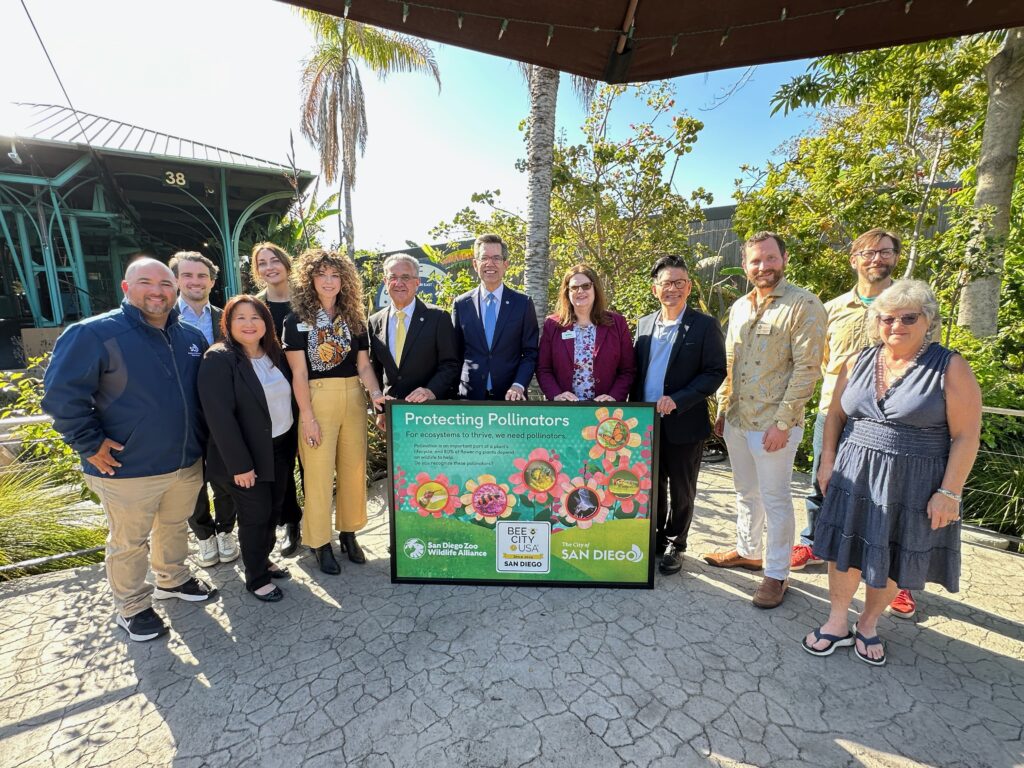 A group of 12 smiling people stand outside with a large interpretive sign.