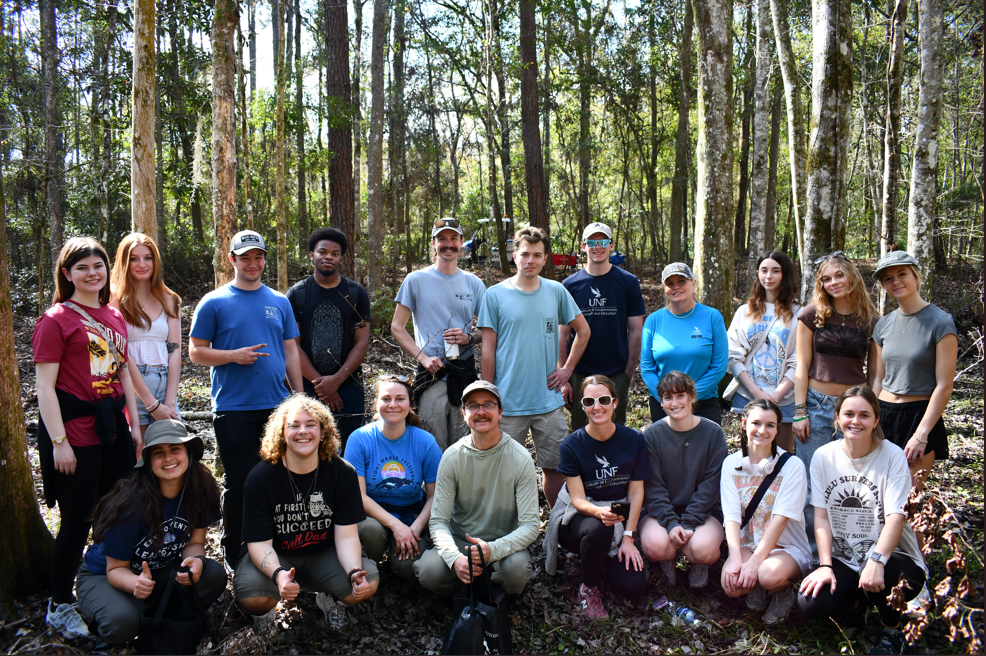 Around 20 people pose in tow rows in a forest.