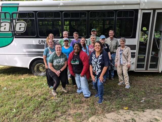 Over a dozen people pose in front of a bus.