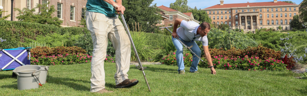 2 people manually aerate a lawn.