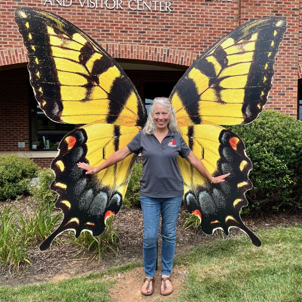 A person smiles in front of large sculpture of yellow swallowtail butterfly wings.