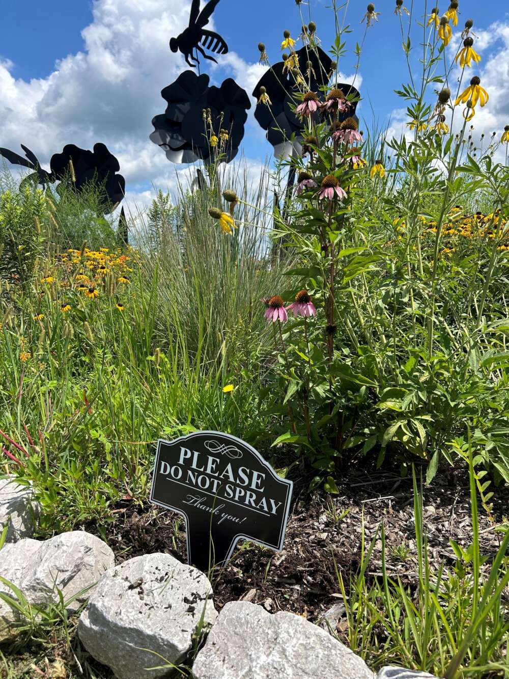 A flowering garden with a sign reading "Please do not spray. Thank you!"