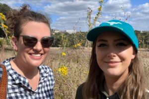 Two people smile in front of yellow flowers.