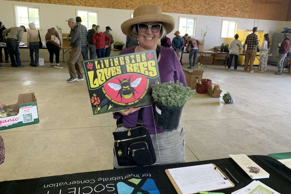 A person smiles holding up a yard sign inside a large building.