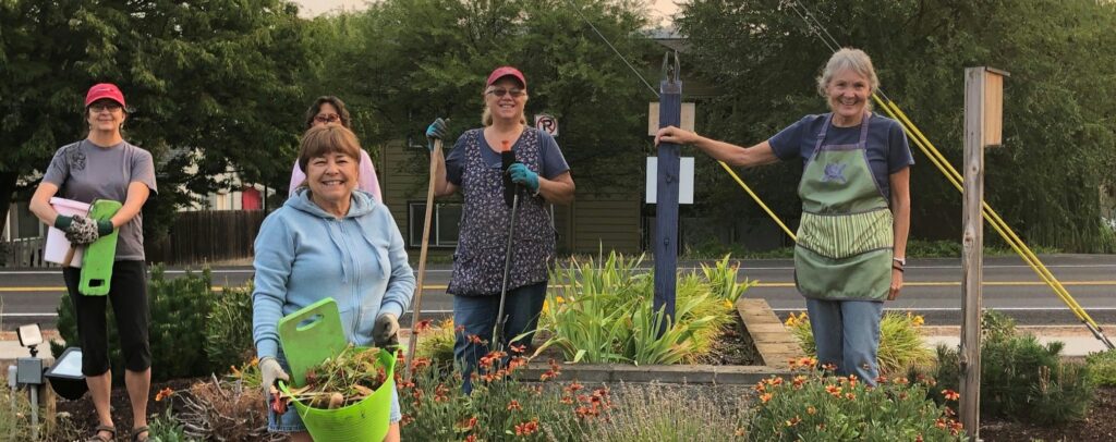 People stand around a flowering garden with garden tools.