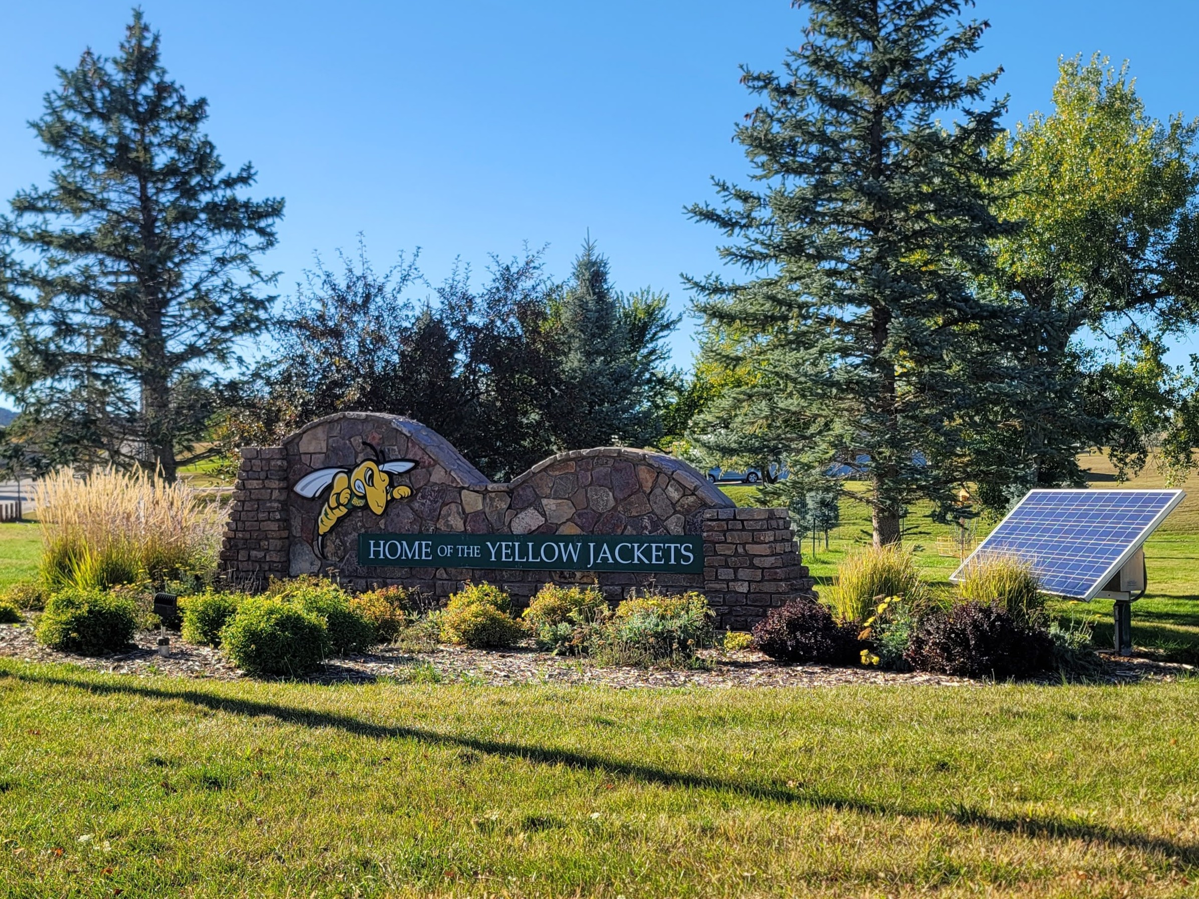 A large stone sign with a cartoon yellowjacket with a solar panel off to the side.