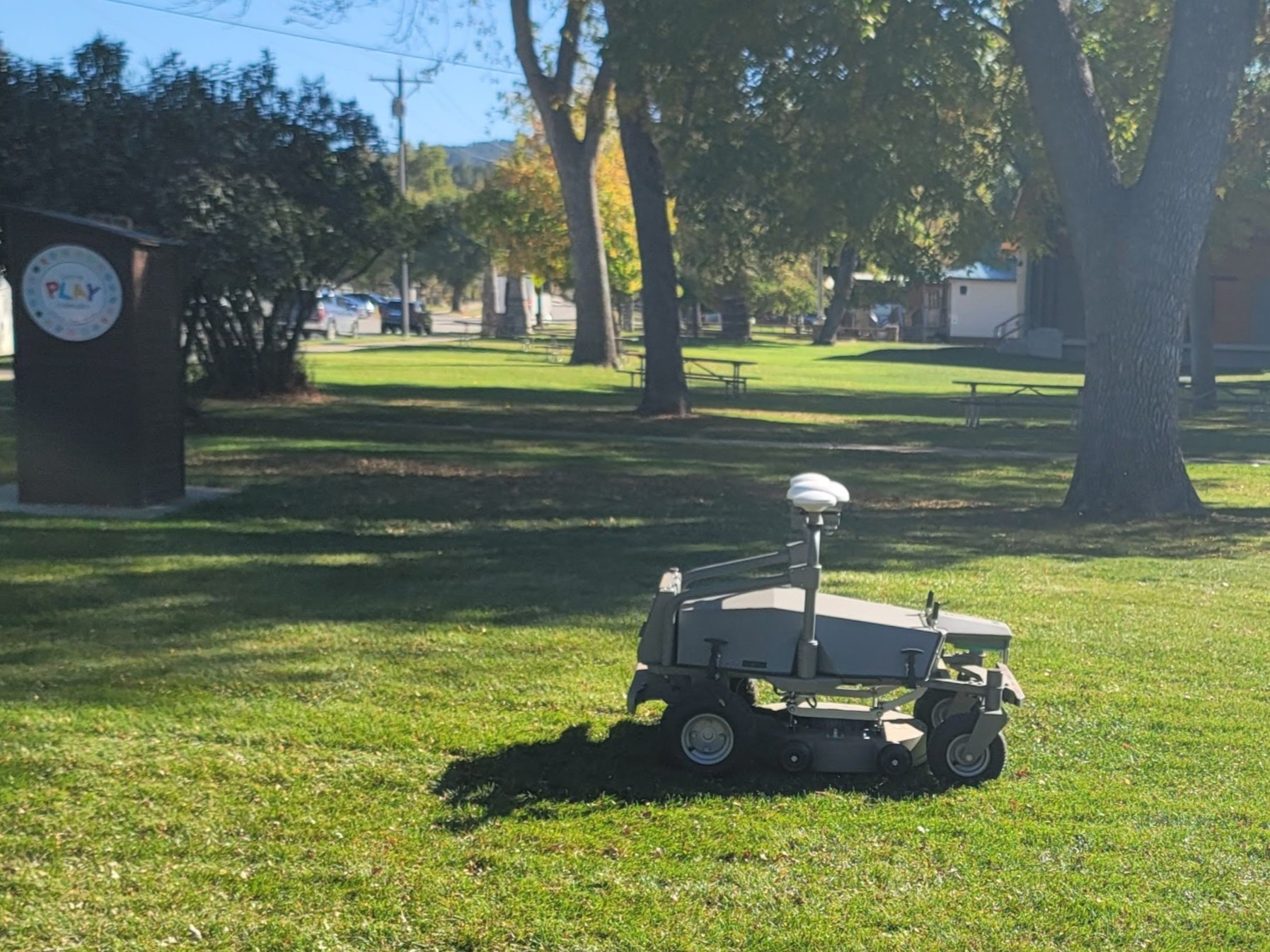 A small four-wheeled mowing vehicle in a green park.