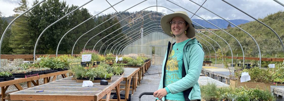 Woman in sun hat stands in a greenhouse full of plants