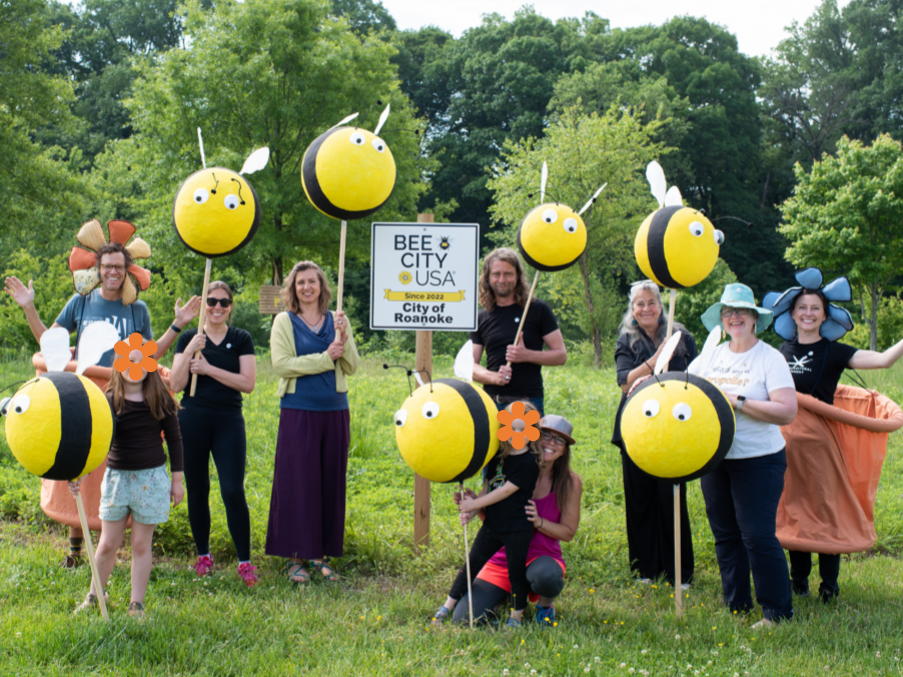 A group holding up model bumble bees on posts around a Bee City USA sign