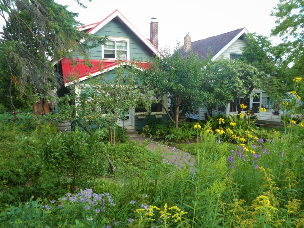 A green garden with flowers in front of a teal house with a red roof.