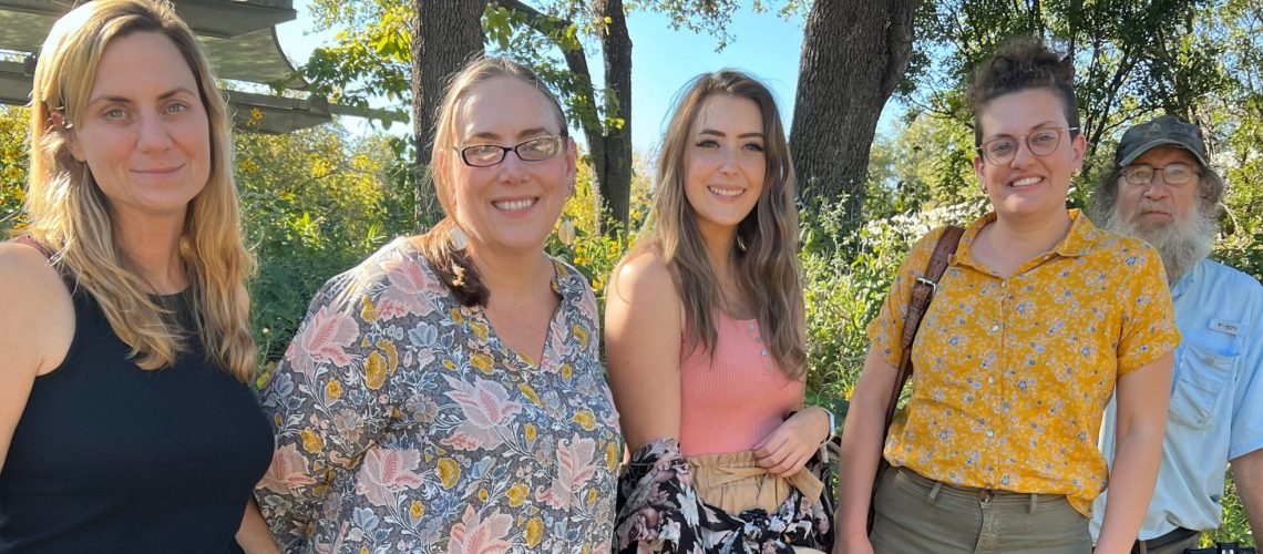 Five people smile in front of yellow flowers.