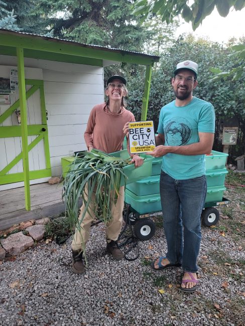 Two people smile holding vegetables and a small sign.