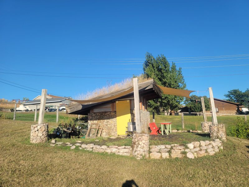 A small shed with chairs and a low stone wall.