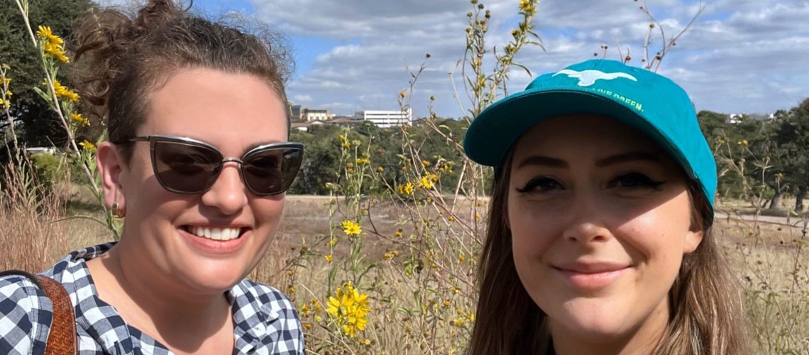 Two people smile on a sunny day with yellow flowers and yellow grass in the background.