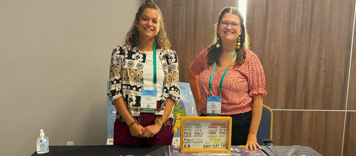 Two people stand smiling behind a table indoors.